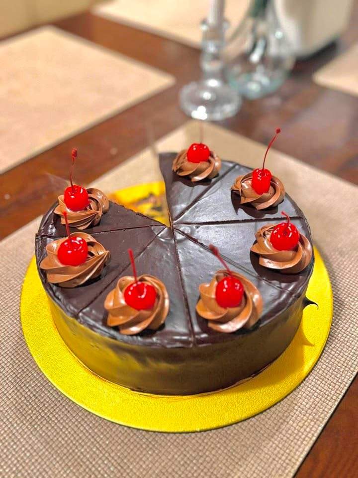 A chocolate cake topped with piped cream and cherries