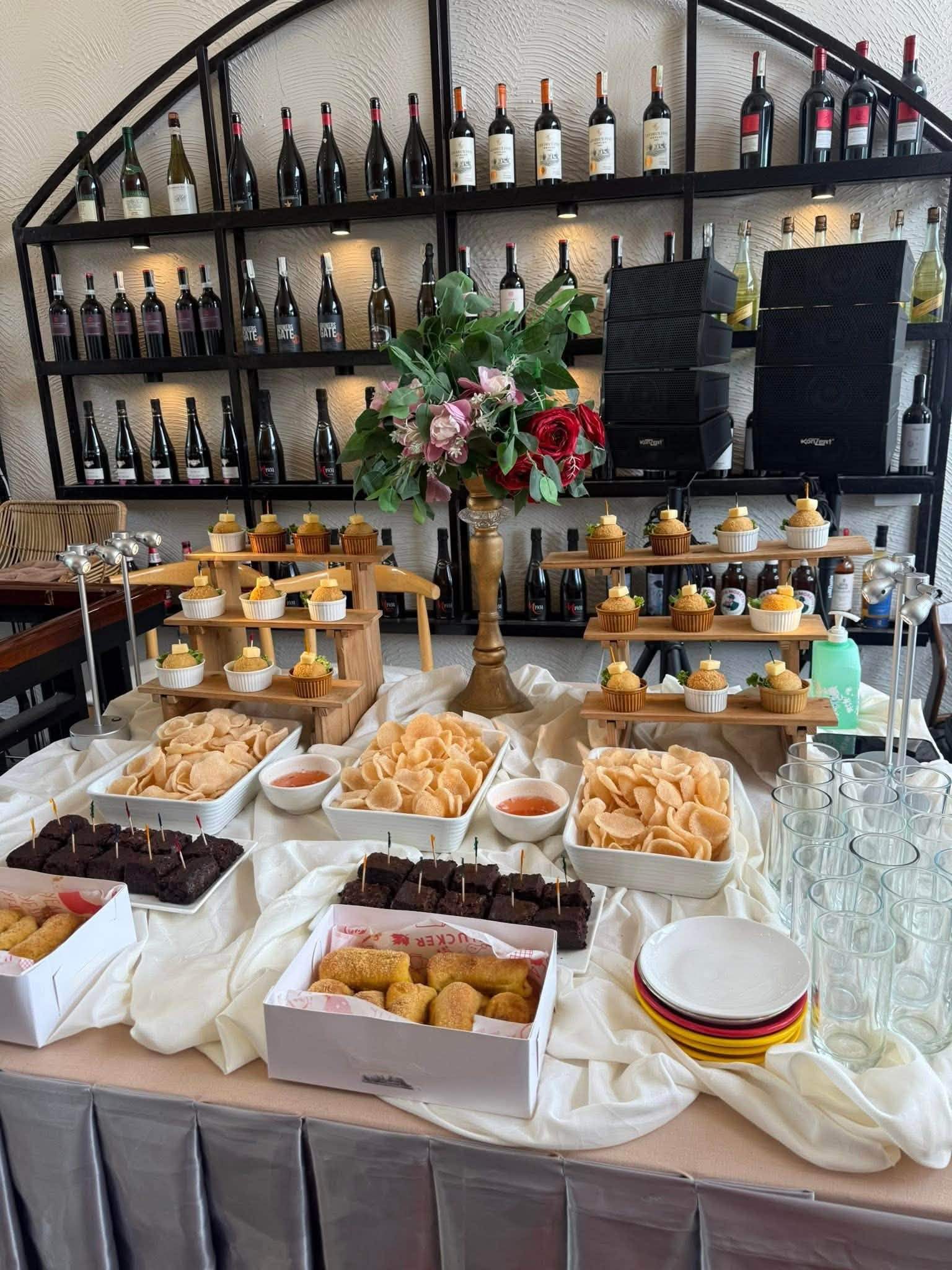 A dessert table of cakes, pastries and sweets in front of the wine shelves