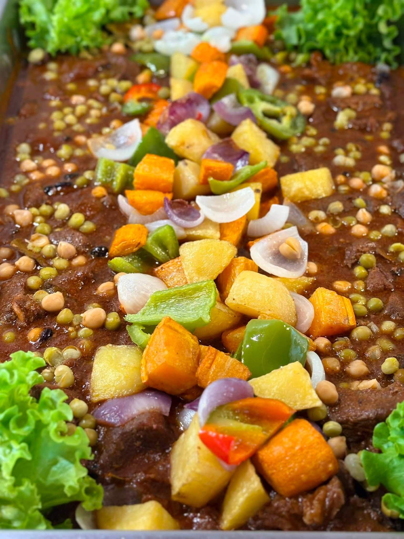 A rich tomato stew topped with potatoes, carrots, bell peppers, onions and peas