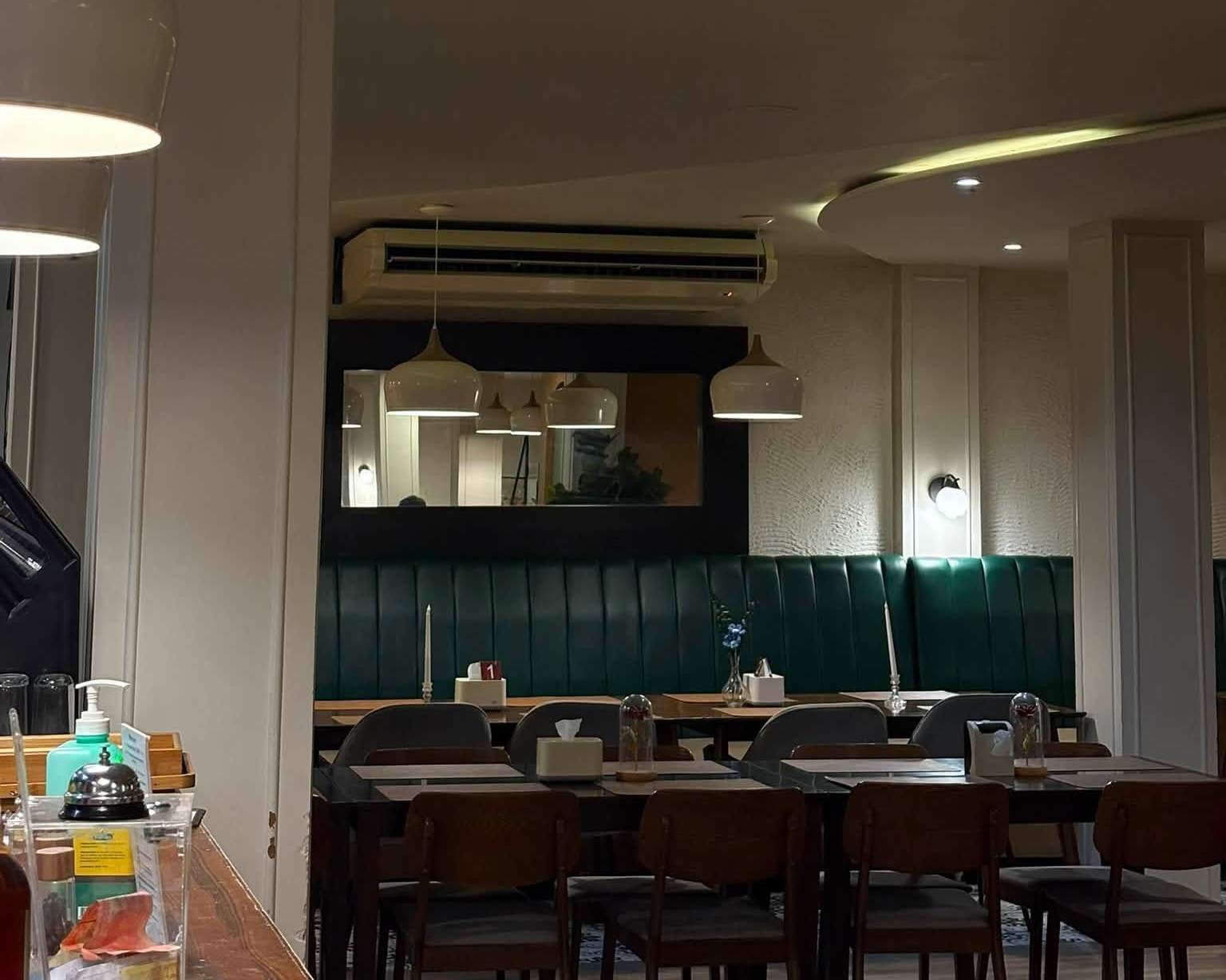 Dining room with green tufted banquettes, white pendant lights and wooden chairs