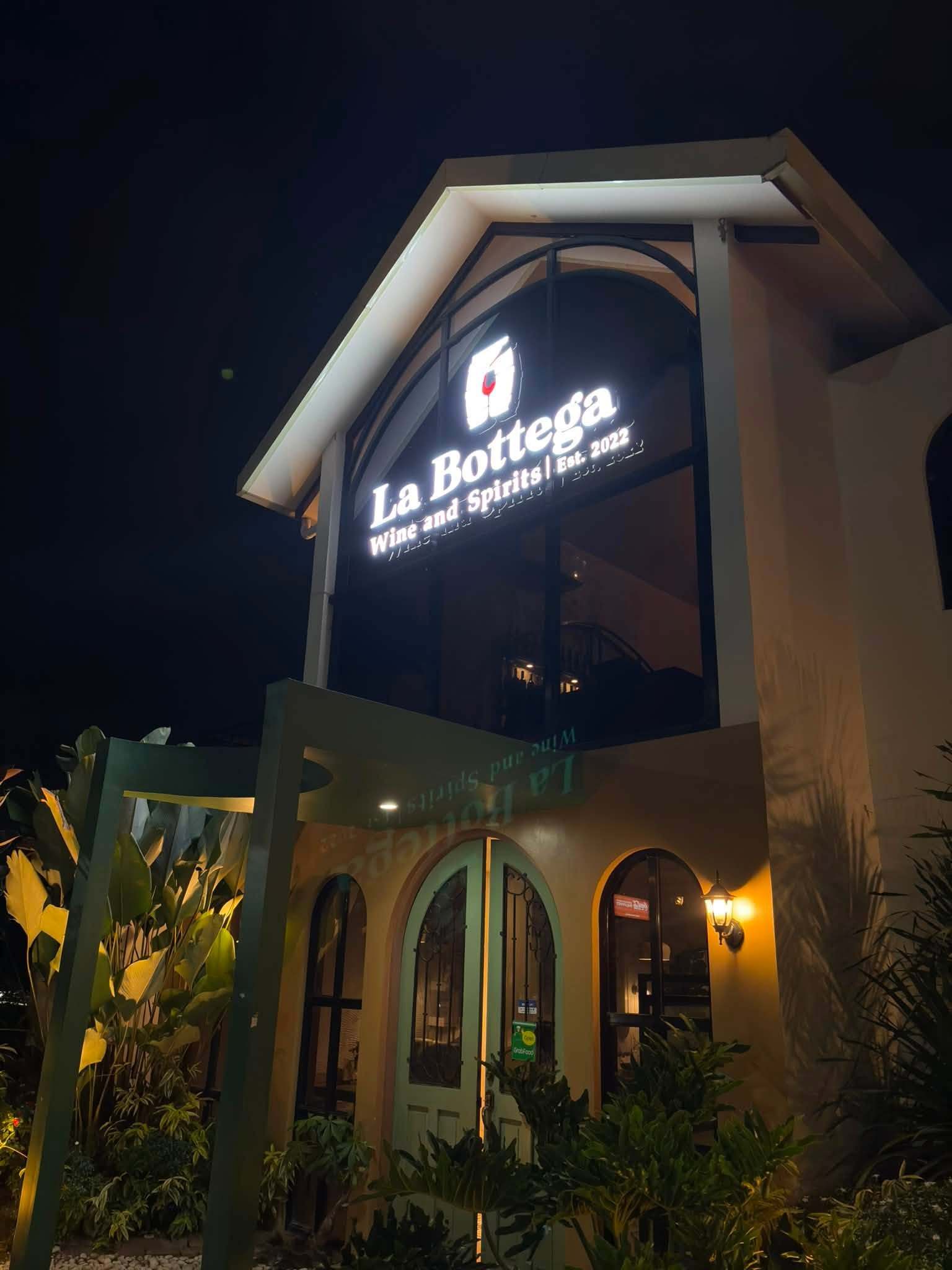 The illuminated La Bottega sign on the gabled facade at night, with warm lanterns at the entrance